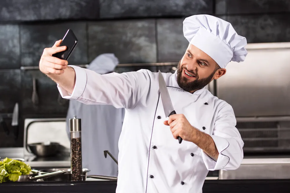 Leende kock tar en selfie med mobilen i ett restaurangkök